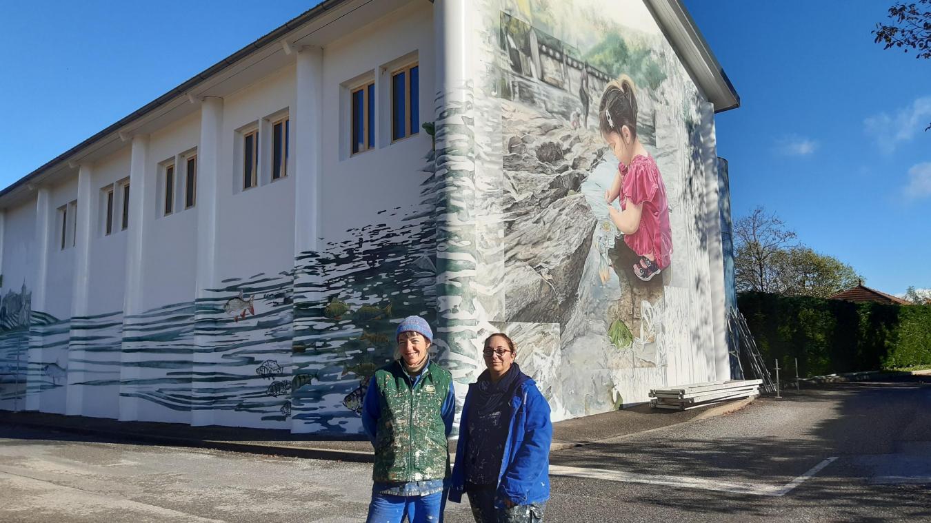 Camille et Mélanie devant leur fresque sur la façade de la salle des fêtes de Billiat.
